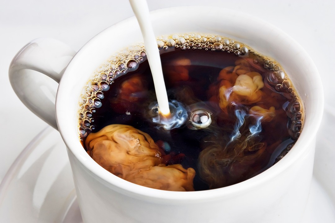 Close up view of creamer pouring into black cup of coffee